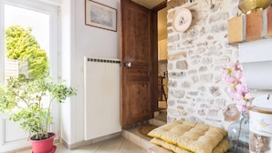 Un intérieur rustique avec un mur en pierre, une porte en bois, un radiateur, une plante en pot et un banc agrémenté de coussins.