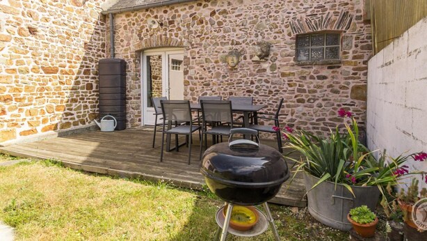 Un bâtiment en pierre doté d’une terrasse en bois, d’un espace extérieur aménagé pour s’asseoir et d’un barbecue.