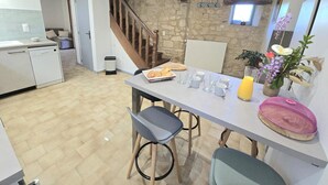 A modern kitchen with a stone wall, wooden staircase, and a dining area with chairs and a table set for breakfast.