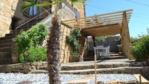 A stone building with a wooden pergola and a palm tree in the foreground.