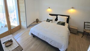 A bedroom with a bed, bedside tables, a chair, a small table with a bowl and remote, and a window with curtains.