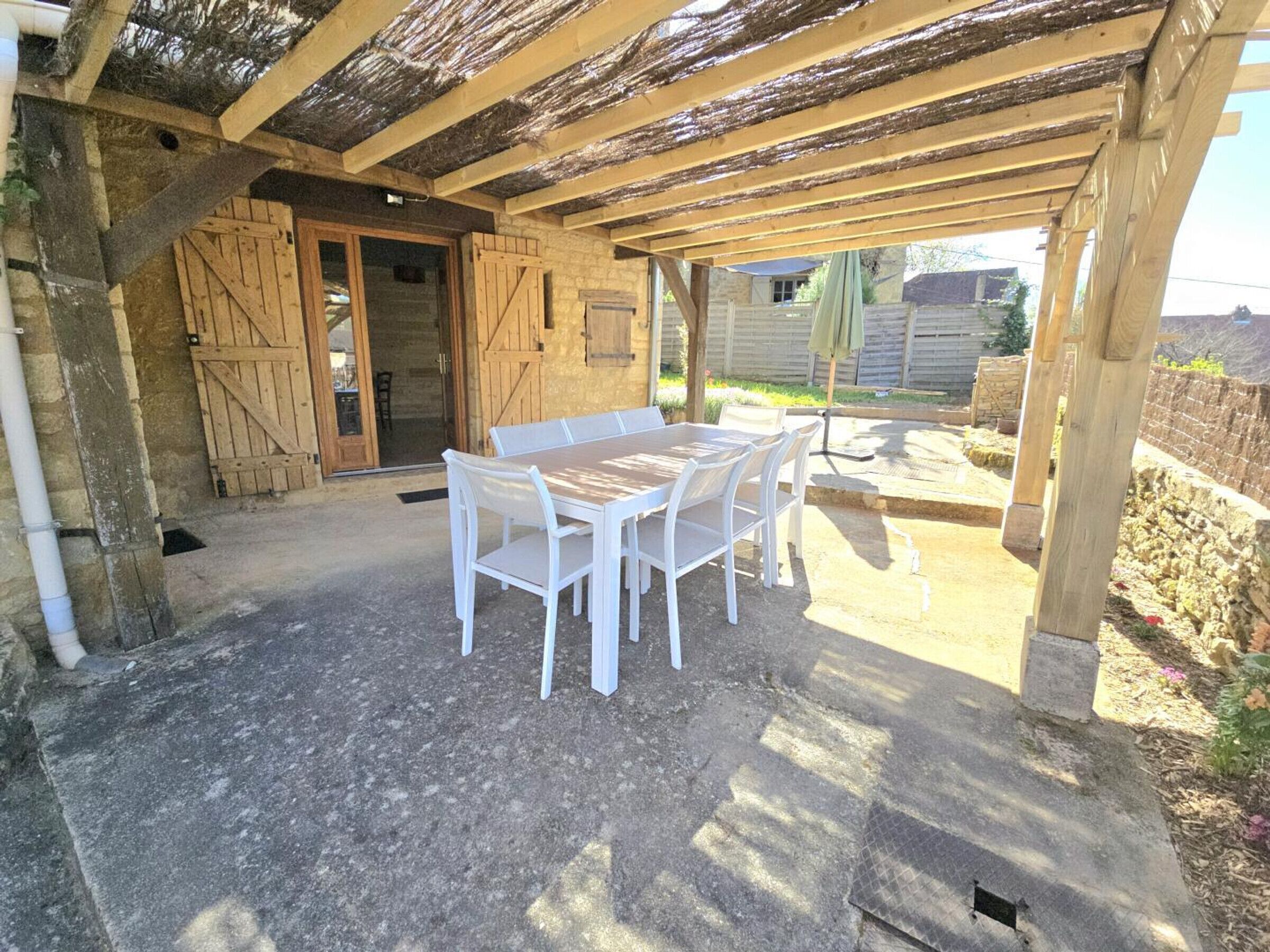 Une terrasse extérieure avec une table et des chaises en bois, un espace couvert avec un plafond en bois et un mur de pierre en arrière-plan.