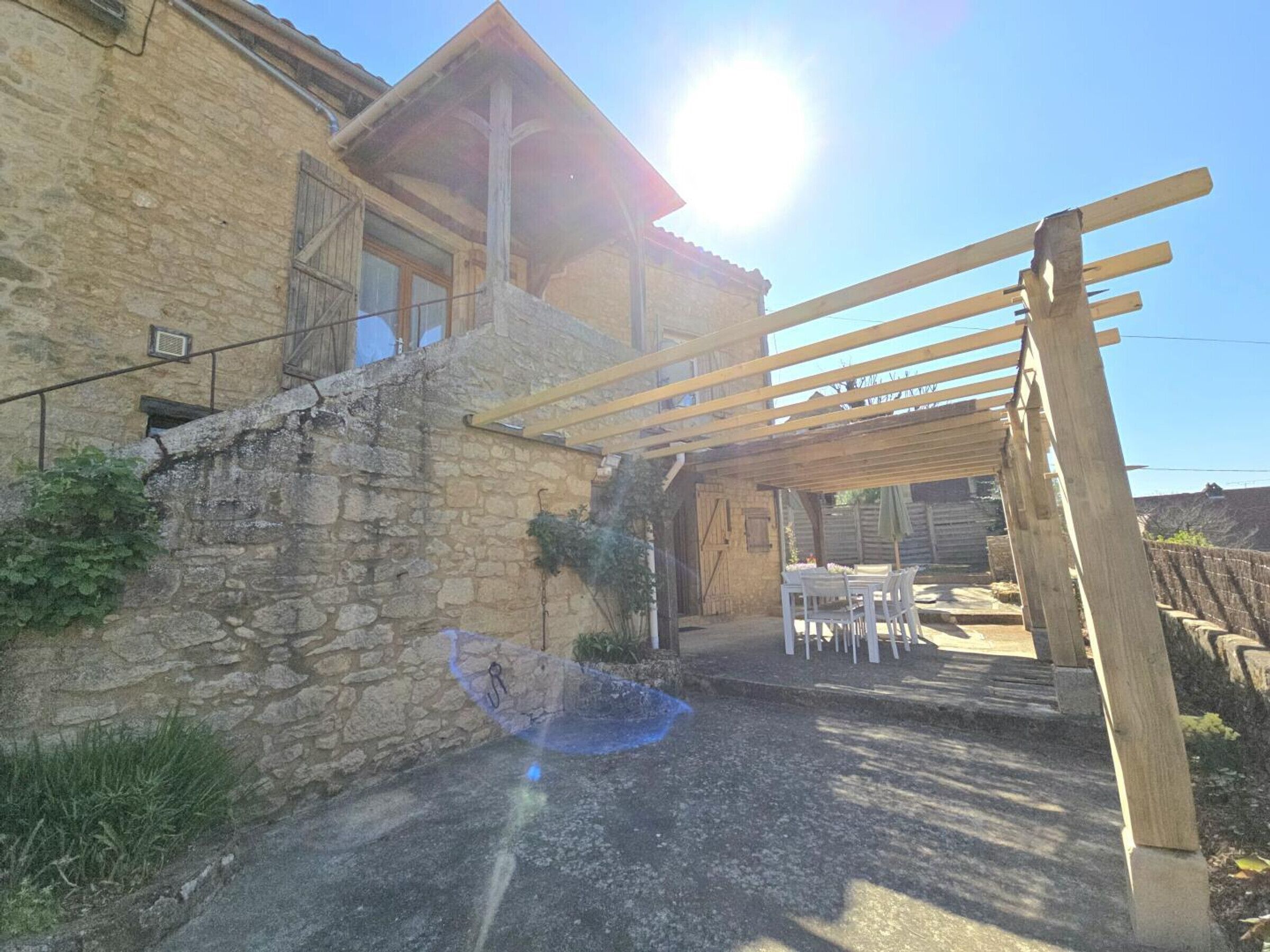 Edificio de piedra con una pérgola de madera y un patio con muebles de exterior.