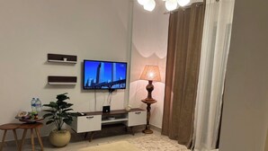 Un saló amb televisió de pantalla plana, una làmpada, un sofà i una taula petita amb una planta.