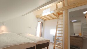 A bedroom with two beds, a wooden ladder, and a bathroom with a mirror and sink.
