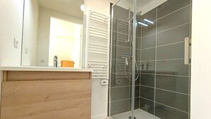A modern bathroom with a glass shower enclosure, a wooden vanity, and a large mirror.