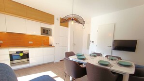 A modern kitchen with white cabinets, a microwave, and a built-in oven. There is a dining table with chairs and a TV mounted on the wall.