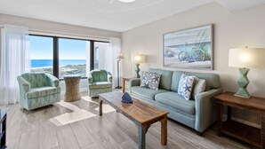Een woonkamer met uitzicht op het strand, een bank, twee fauteuils, een salontafel en twee lampen.