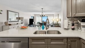 Een moderne keuken met een roestvrijstalen spoelbak, houten keukenkastjes en uitzicht op de woonkamer.