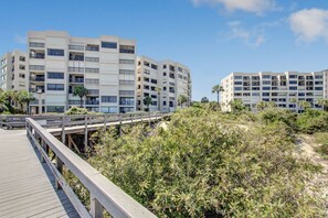 Ein Strandhotel mit mehreren Etagen, einer Holzpromenade und dichter Vegetation.