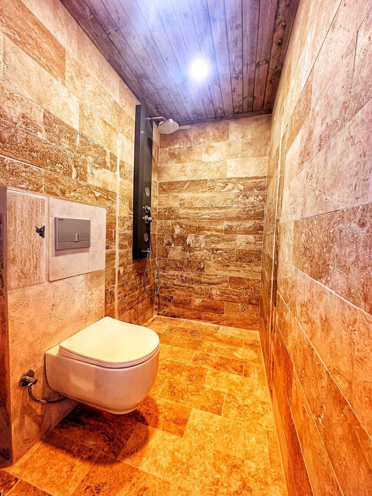 Un baño con pared de piedra, inodoro y zona de ducha.