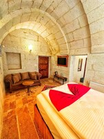 Una habitación acogedora con techo de arco de piedra, un sofá de madera, una cama con manta roja y una mesita con hervidor.