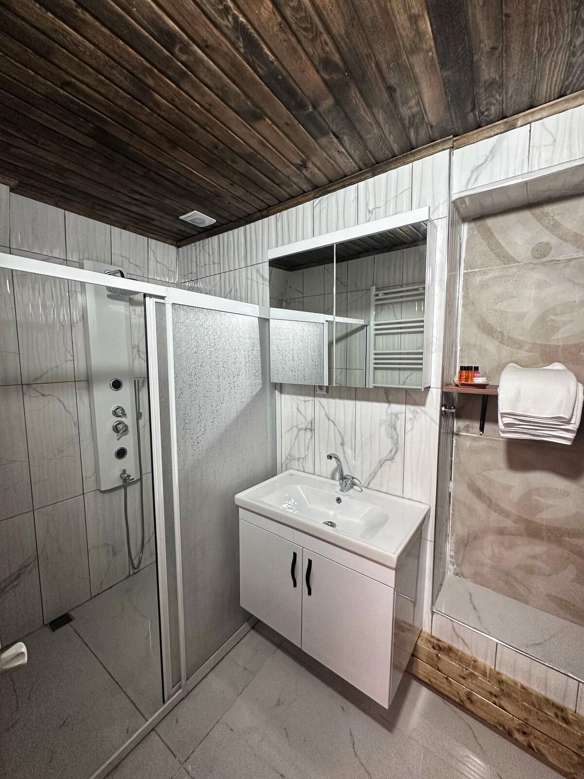 Ein modernes Badezimmer mit Duschkabine aus Glas, einem weißen Waschtisch mit Marmor-Spritzschutz und einer Holzbodenverkleidung.