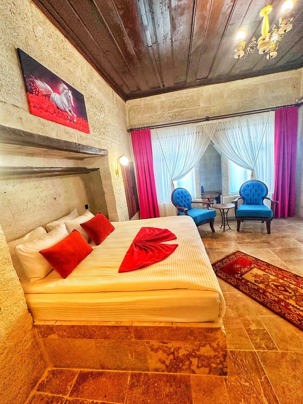 A hotel room with a bed, two blue armchairs, a small table, and a chandelier.