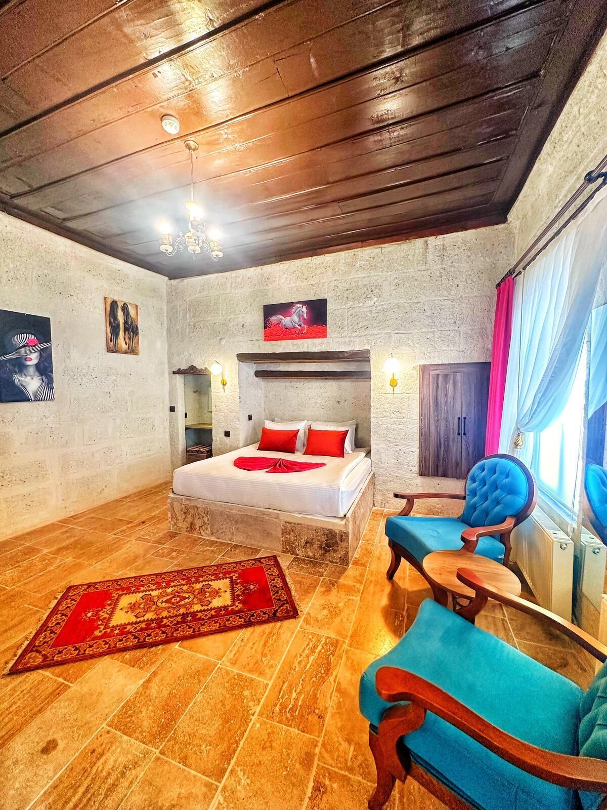 A bedroom with a bed, a blue armchair, a red rug, and artwork on the walls.