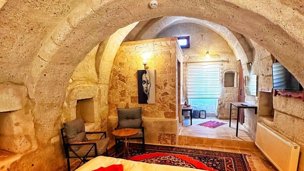 A cozy, stone-walled room with a bed, a small table, and a chair. - CRİMSON CAPPADOCİA (Avanos)