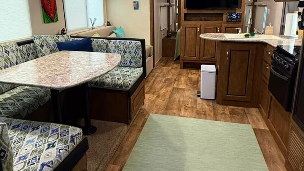 Interior compacto de una caravana con kitchenette, zona de comedor con mesa redonda y área de estar con cojines estampados.