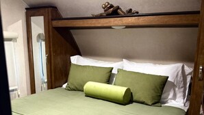 Una cama individual con colcha y almohadas verdes, cabecera de madera y un pequeño adorno en la cabecera.