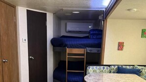 Interior compacto de una autocaravana con literas, una kitchenette pequeña y un armario de almacenamiento.