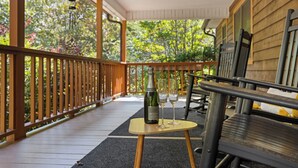 Une terrasse en bois avec une table sur laquelle se trouvent une bouteille et deux verres, entourée de chaises.