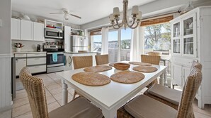 A modern kitchen with white cabinets, a microwave, and a dining area with a white table and wicker chairs. - BAY Views/Community Pool - 1 Port Lewes (Lewes)