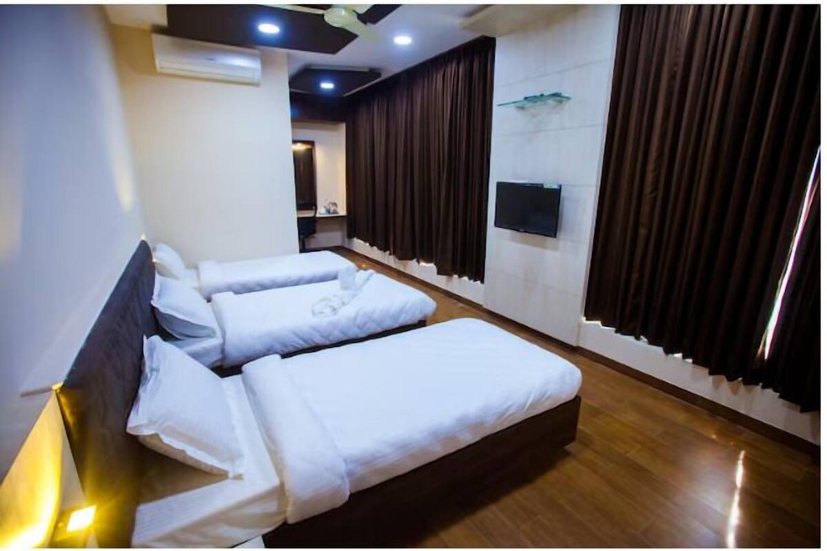 A hotel room with two beds, a flat-screen TV, and a large window with curtains.