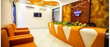 Zona de recepción con asientos naranjas, un arreglo floral y un letrero que dice 'GRACE' en la pared.