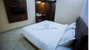 A hotel room with a bed, a TV mounted on the wall, a desk with a chair, and a wardrobe. - Twilight Inn (Chennai)