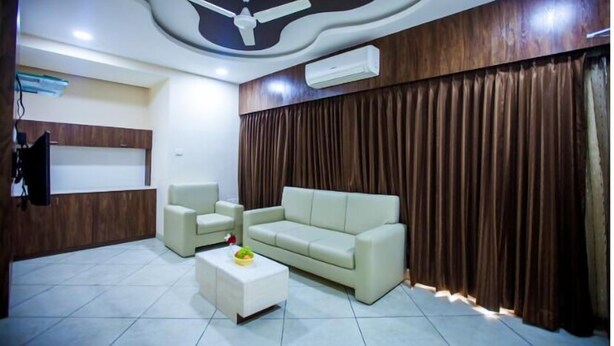 A modern living room with a beige sofa, two armchairs, a coffee table, a ceiling fan, and a large window with curtains. - Twilight Inn (Chennai)