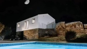 Et moderne hus med pool, stenvæg og en stor klippeformation.