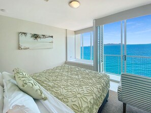 A bedroom with a bed, pillows, a window, and a view of the ocean.