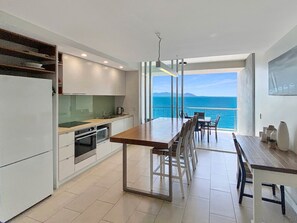 A modern kitchen with a dining area, large windows, and a view of the sea. - 1 Bright Point Apartment 4305 (Nelly Bay)