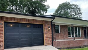 A two-story brick building with a large garage door, a covered porch with a window, and a small front yard. - Lovely 3-bedroom house with AC in vibrant Atlanta (Atlanta)