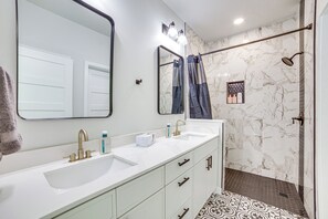 A bathroom with two sinks, a large mirror, and a shower area with a marble wall.