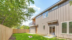 A modern two-story house with a wooden deck, a fenced backyard, and a small patio area.
