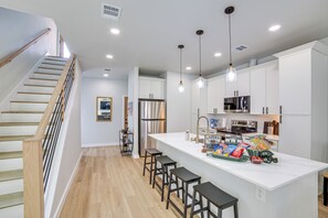 A modern kitchen with a central island, bar stools, stainless steel appliances, and a wooden staircase.