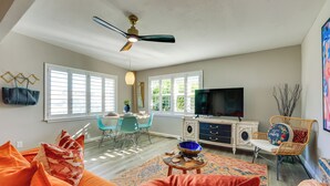 A spacious living room with a large sofa, a television, and a dining area with chairs. - 5 Blocks to Jax Beach: Getaway w/ Patio & Yard! (Jacksonville Beach)
