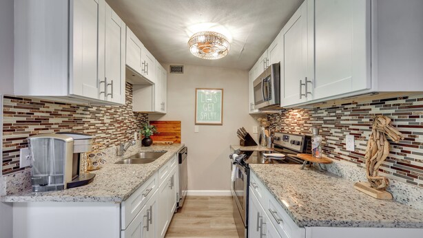 A modern kitchen with white cabinets, a granite countertop, a coffee maker, and a microwave. - 5 Blocks to Jax Beach: Getaway w/ Patio & Yard! (Jacksonville Beach)