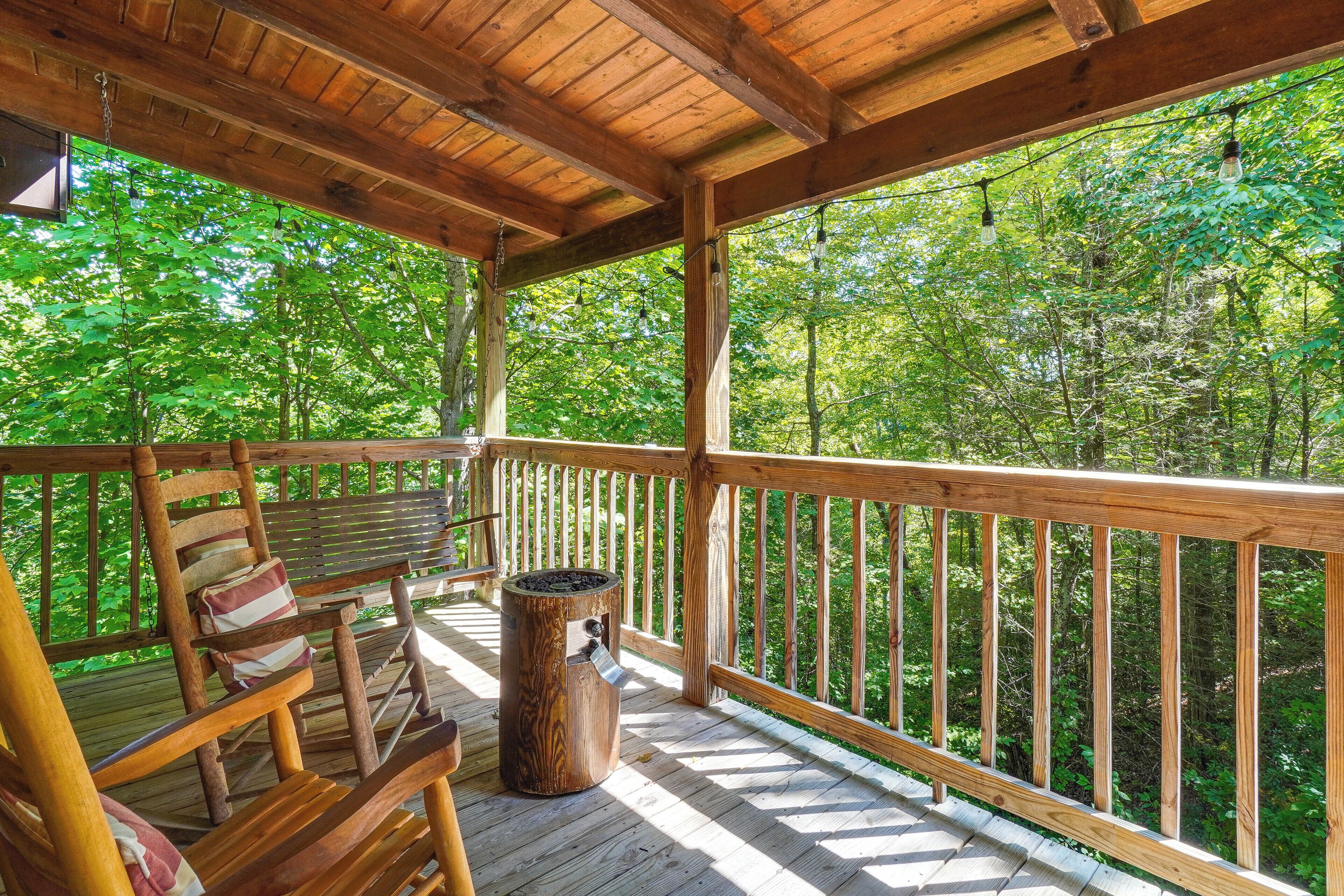A wooden deck with a bench and a trash can, surrounded by a wooden railing, overlooking a forested area.