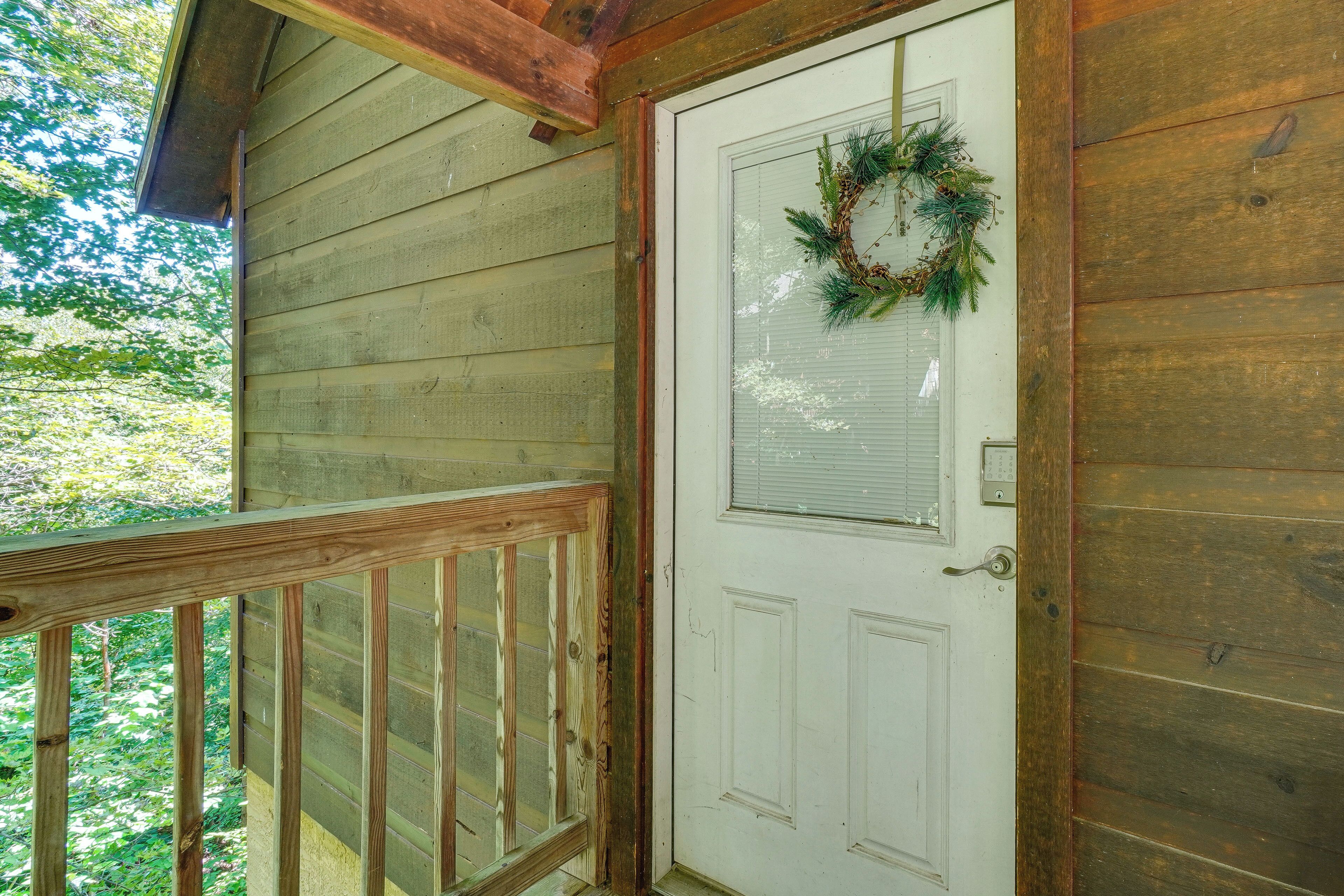 A wooden door with a white panel and a wreath, a wooden railing, and a window with blinds.