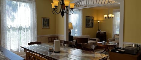 A dining area with a wooden table, chairs, and a chandelier. There are two paintings on the walls and a staircase leading to another level.