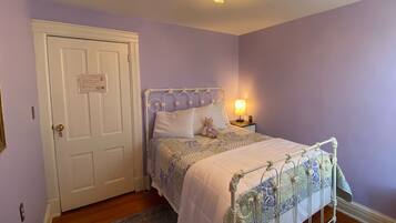 A bedroom with a white door, a bed with a metal frame, a nightstand with a lamp, and a purple wall.