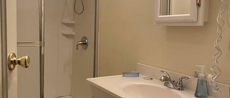 A bathroom with a glass-enclosed shower, a sink with a mirror above it, and a white vanity with cabinets.