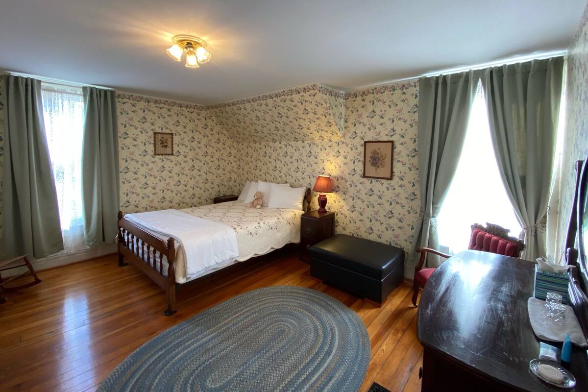 A bedroom with a wooden bed, a nightstand, a lamp, a small table, and a chair.