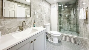 A modern bathroom with a marble vanity, a toilet, and a glass-enclosed shower.