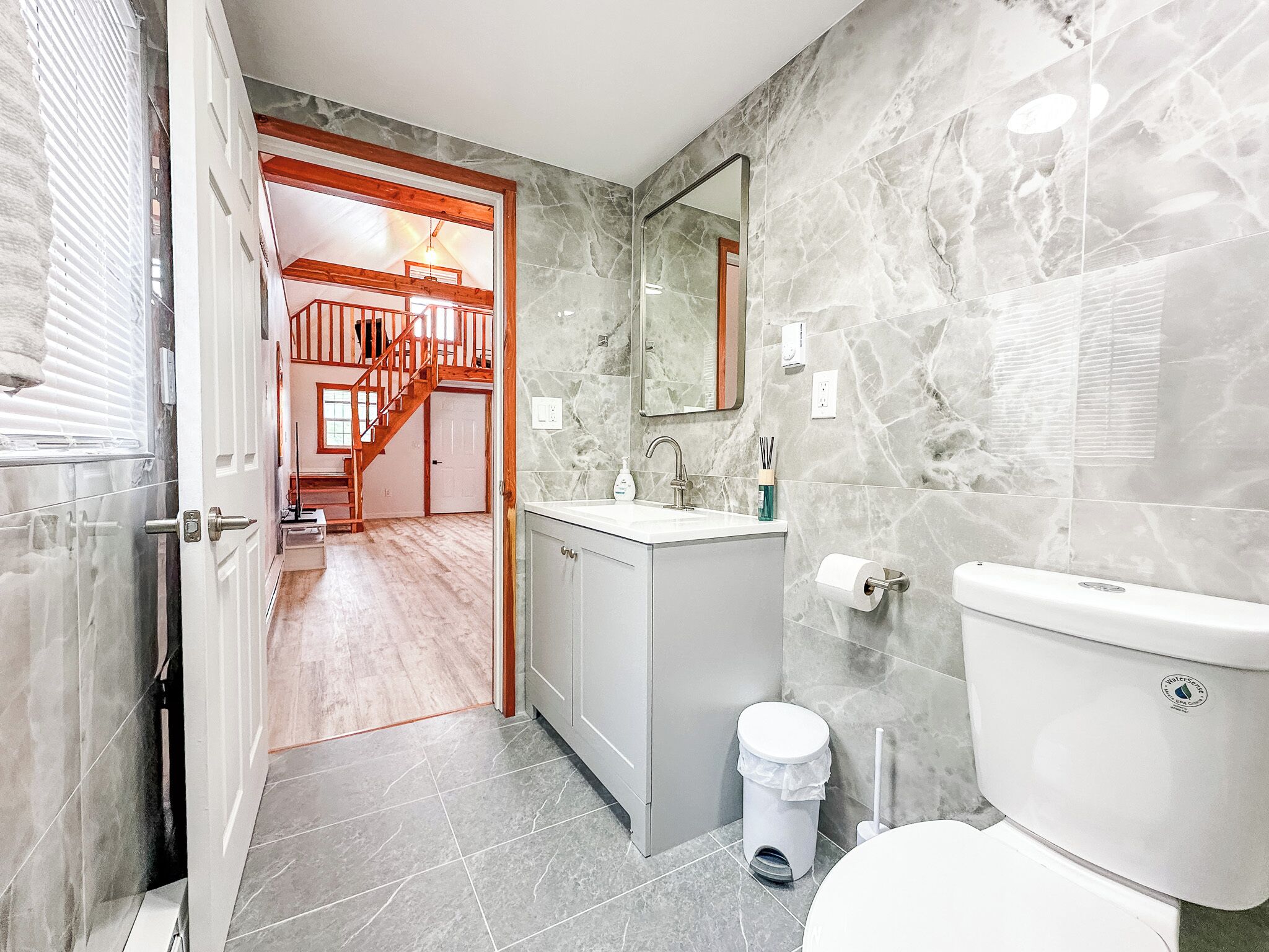 A bathroom with a marble wall, a sink, a toilet, and a trash bin.