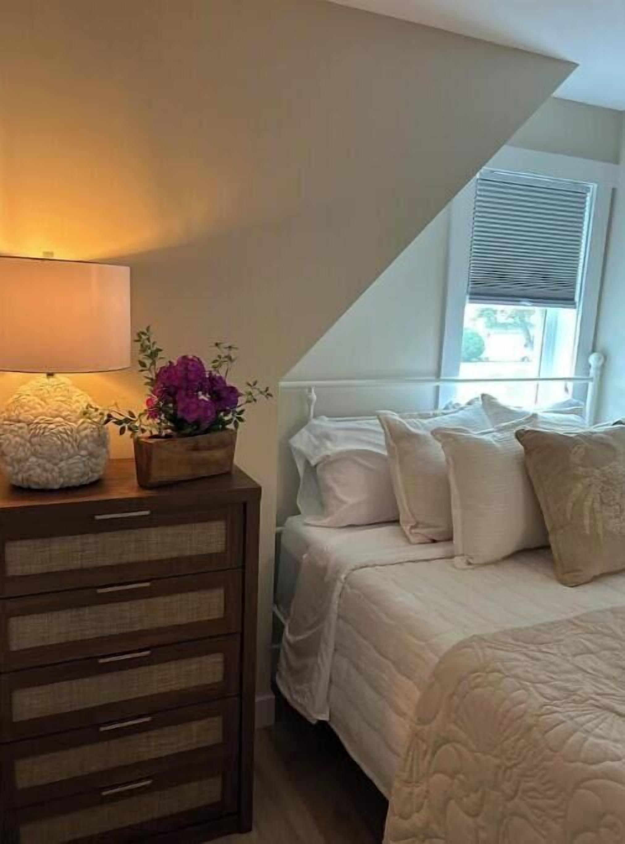 A bedroom with a bed, a nightstand, a lamp, and a window with blinds.