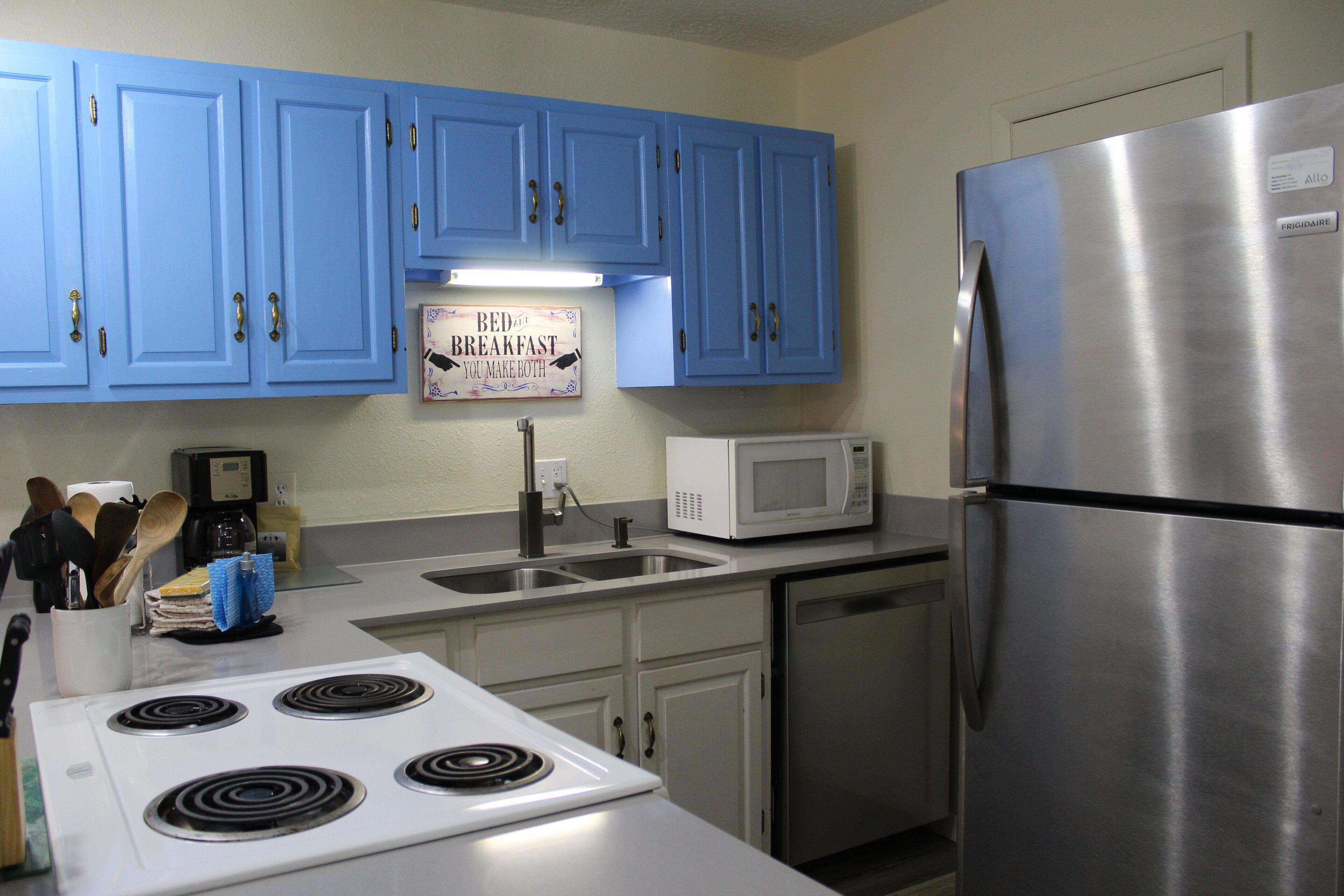 A kitchen with blue cabinets, a stainless steel refrigerator, a microwave, and a stove.