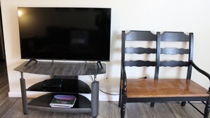 Una TV a schermo piatto su un supporto, con telecomando e un libro poggiato su un tavolinoino di fronte.