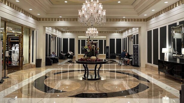 A spacious lobby with a central chandelier, a reception desk, and a circular marble floor.